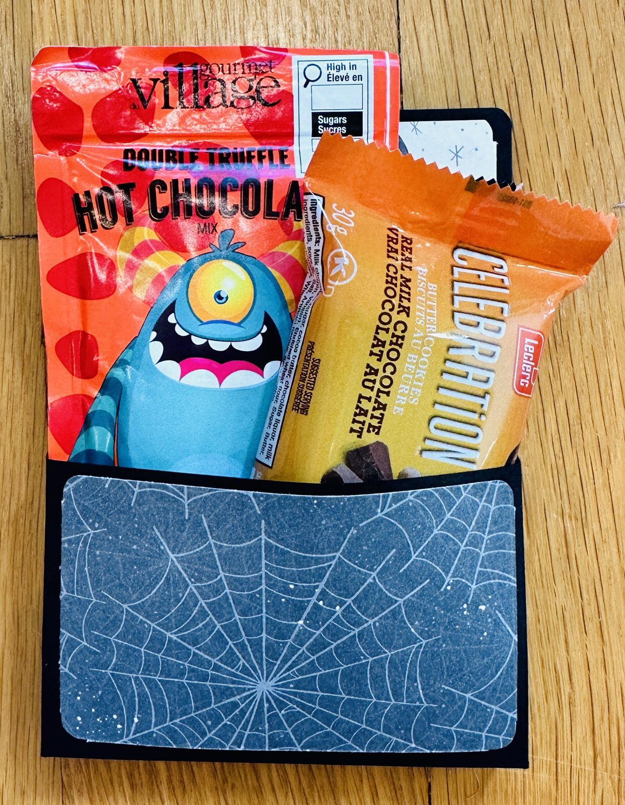 Halloween treat holder card with a spiderweb paper pocket holding a hot chocolate packet and a wrapped butter cookie