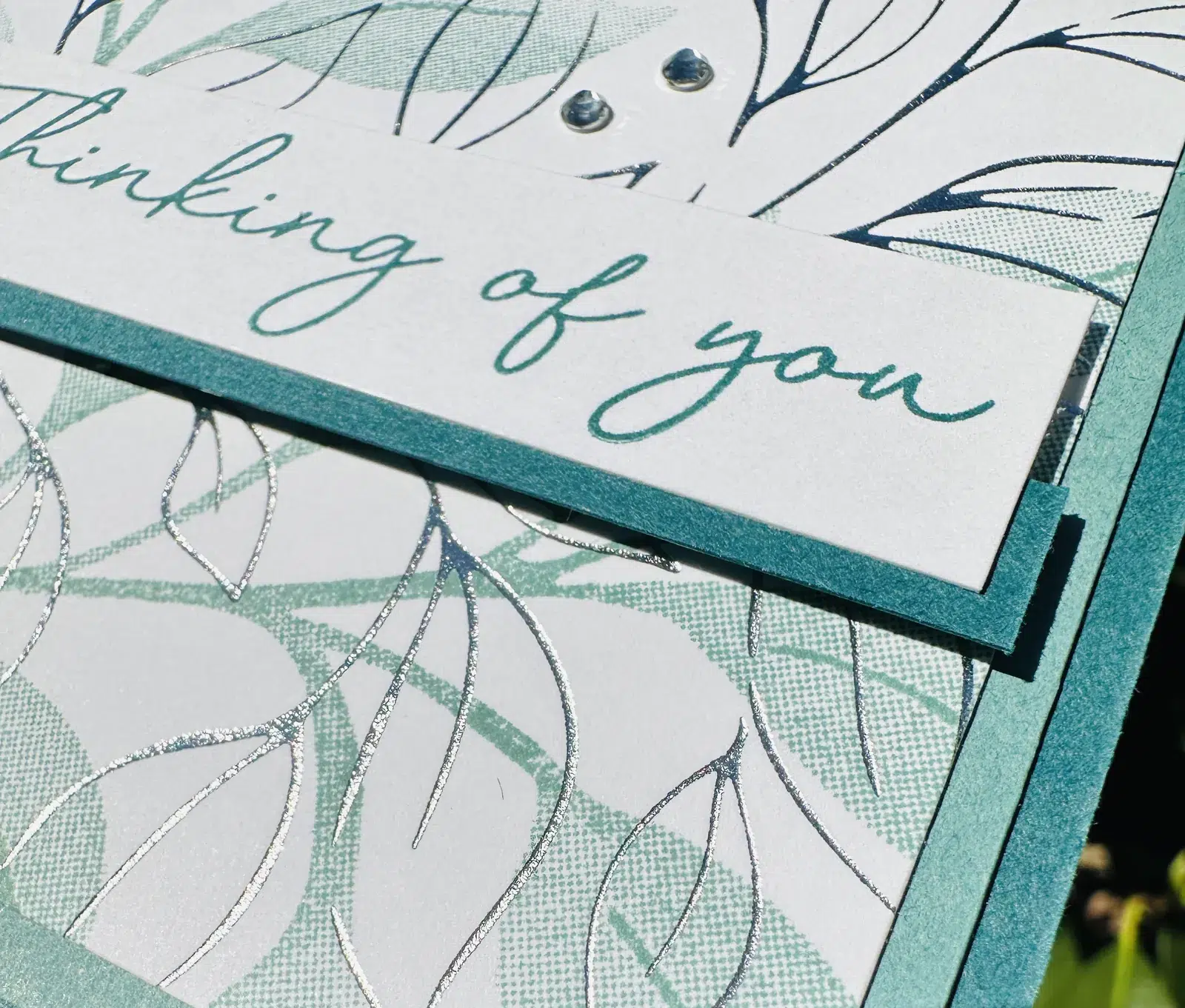 Close-up of silver hot foil leaf details, the Thinking of You sentiment banner and two rhinestone jewels on a hot foil card