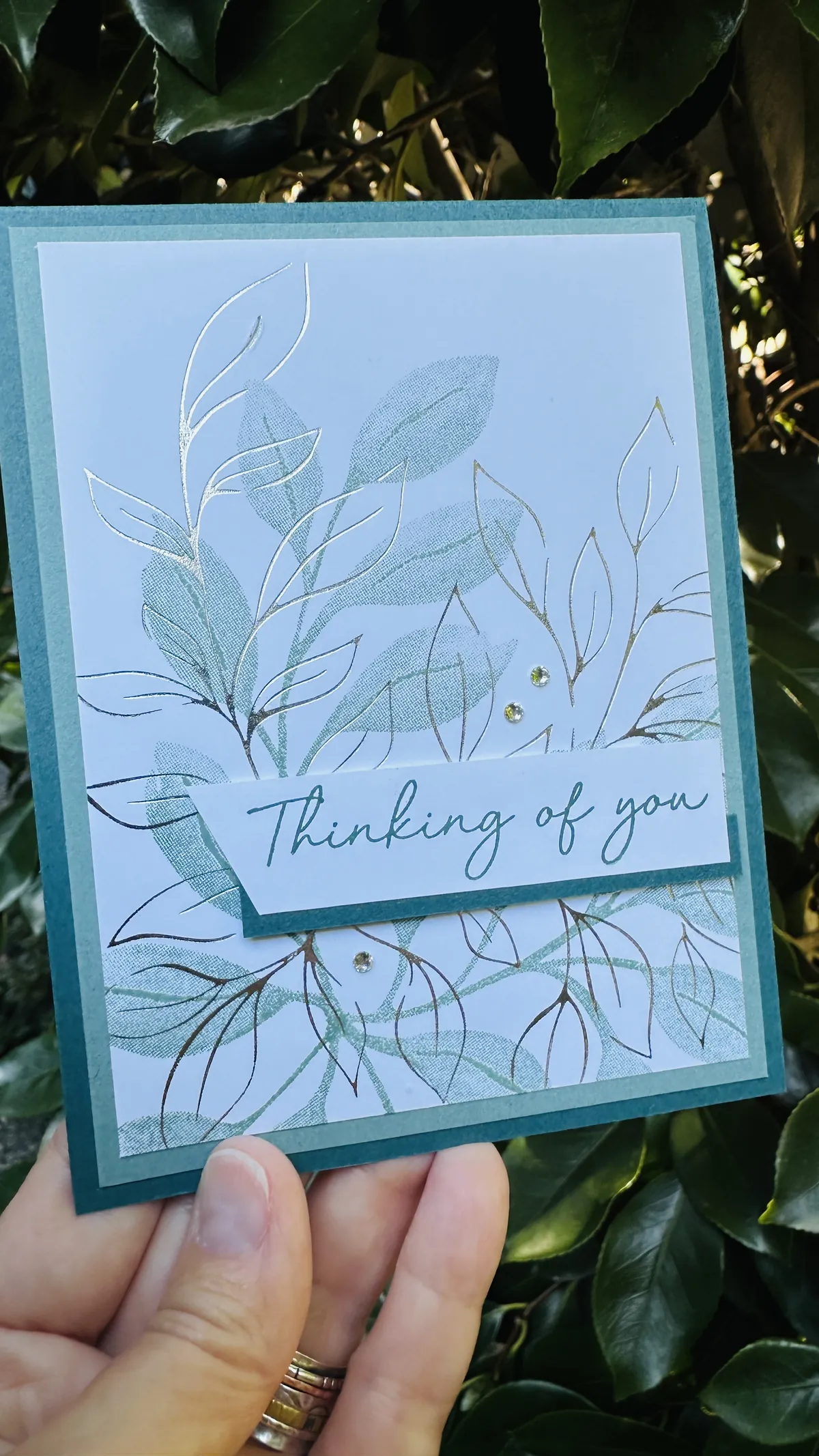 The same hot foil card in warmer light, showing the silver foil leaves catching a bronze shimmer against the Lost Lagoon and Pretty Peacock layers